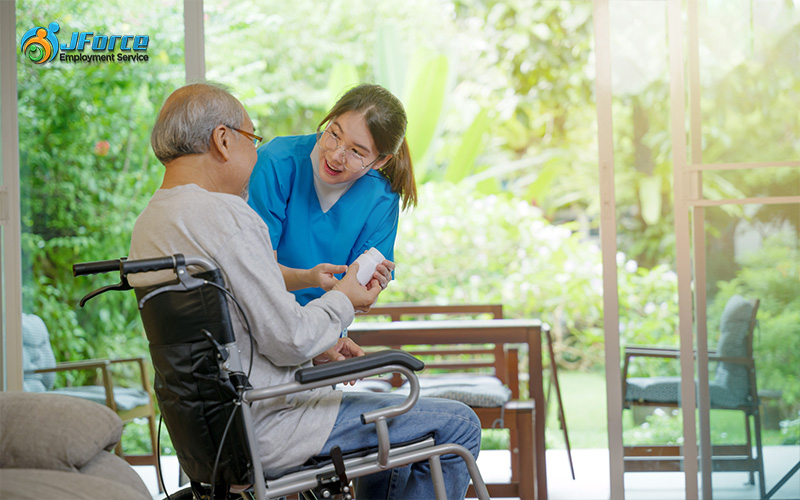 A maid for elderly care gives a bottle of pill to an elderly that sits on a wheelchair.