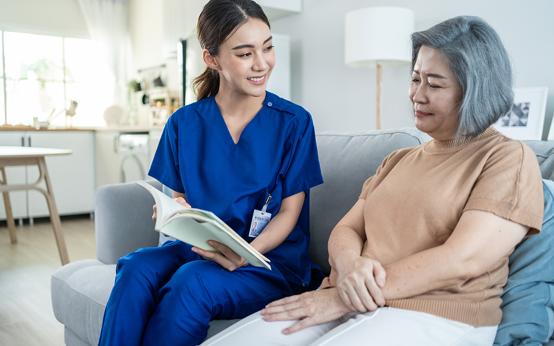 Caregiver reading book to senior woman under Home Caregiving Grant.