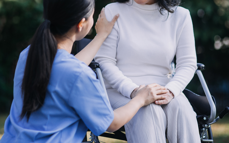 Trained caregiver comforting senior woman in wheelchair in Singapore.