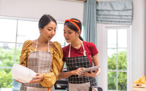 Female employer and domestic helper reviewing recipes on a tablet.